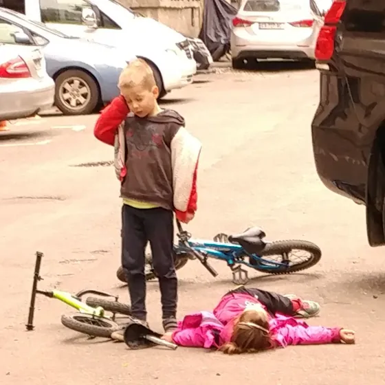 Two children and their bicycles in a courtyard, one lying flat on the asphalt