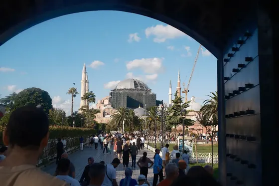 Hagia Sophia and its minarets seen from under a stone archway, crowds crossing the square below